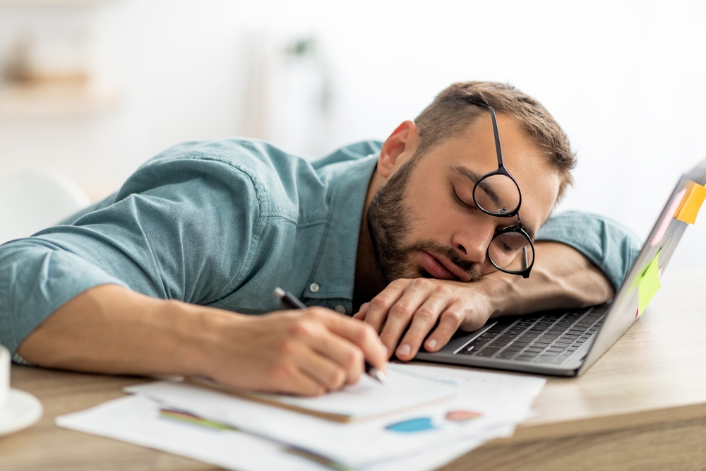 Uomo esausto,Millennial,che,dorme,sulla,scrivania,dell'ufficio,accanto,a